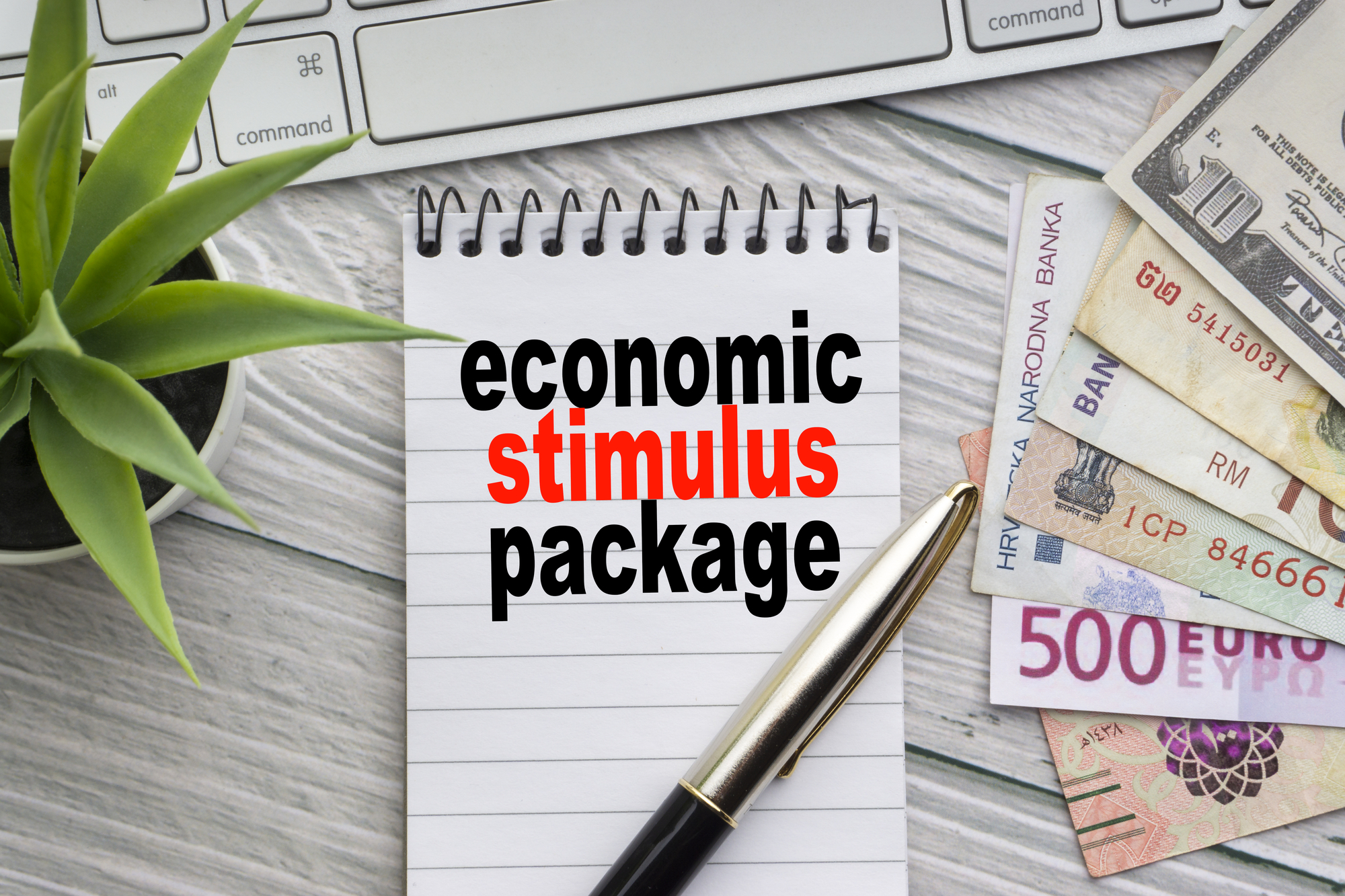 ECONOMIC STIMULUS PACKAGE text with notepad, keyboard, decorative vase, fountain pen, calculator and banknotes currency on wooden background